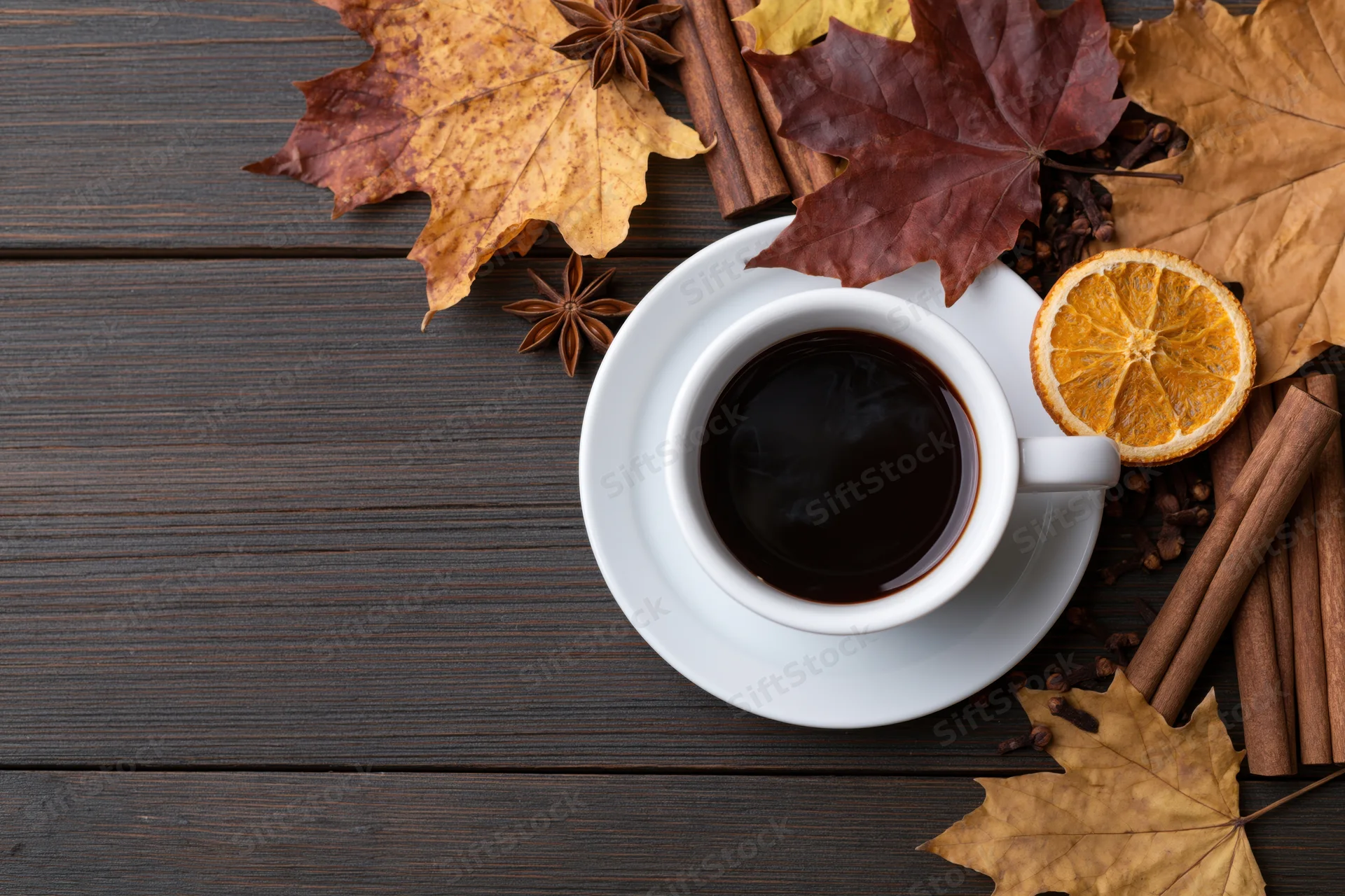 White ceramic coffee cup on saucer surrounded by autumn leaves and spices on dark wooden table