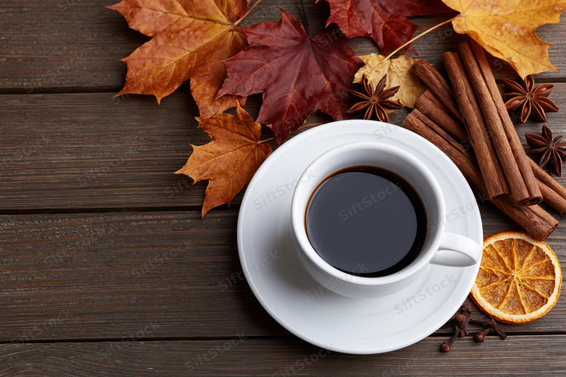 White ceramic coffee cup on saucer with autumn leaves and spices on dark wooden table