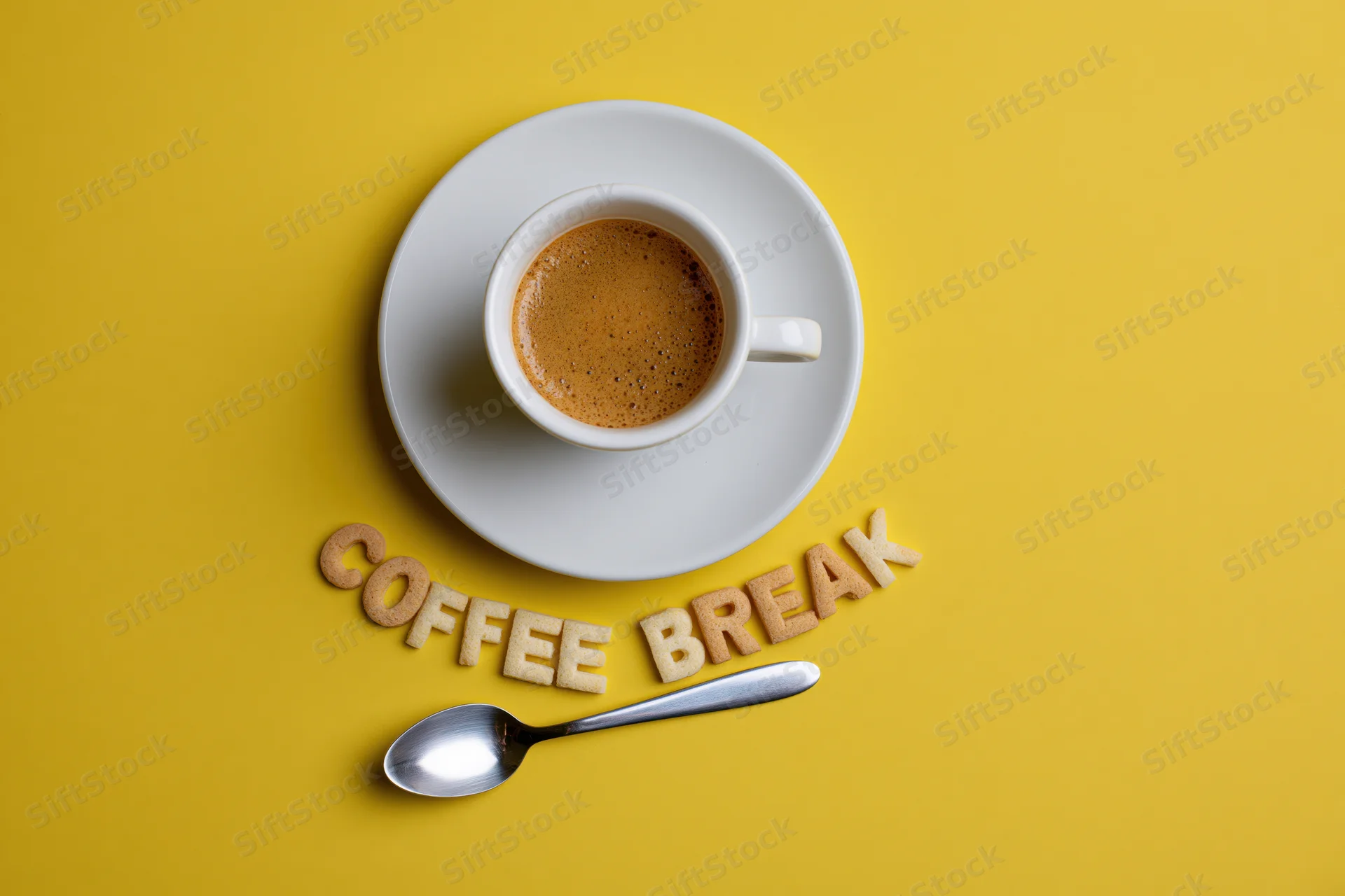 Espresso cup on saucer with cookie letters spelling coffee break and spoon on yellow surface