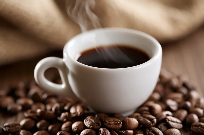 Steaming espresso cup on coffee beans with burlap sack in background