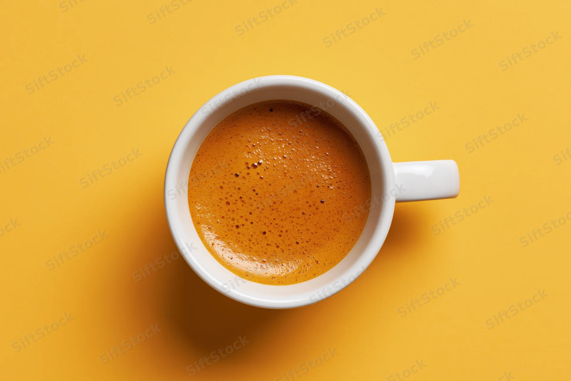 White ceramic espresso cup filled with frothy crema on yellow background, top view