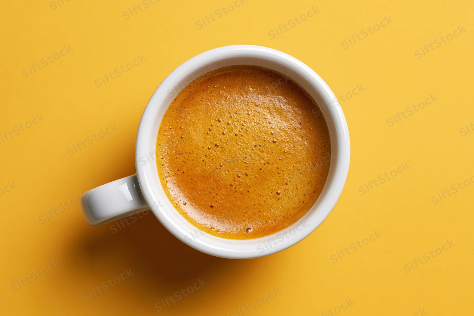 White ceramic espresso cup filled with frothy crema on yellow background