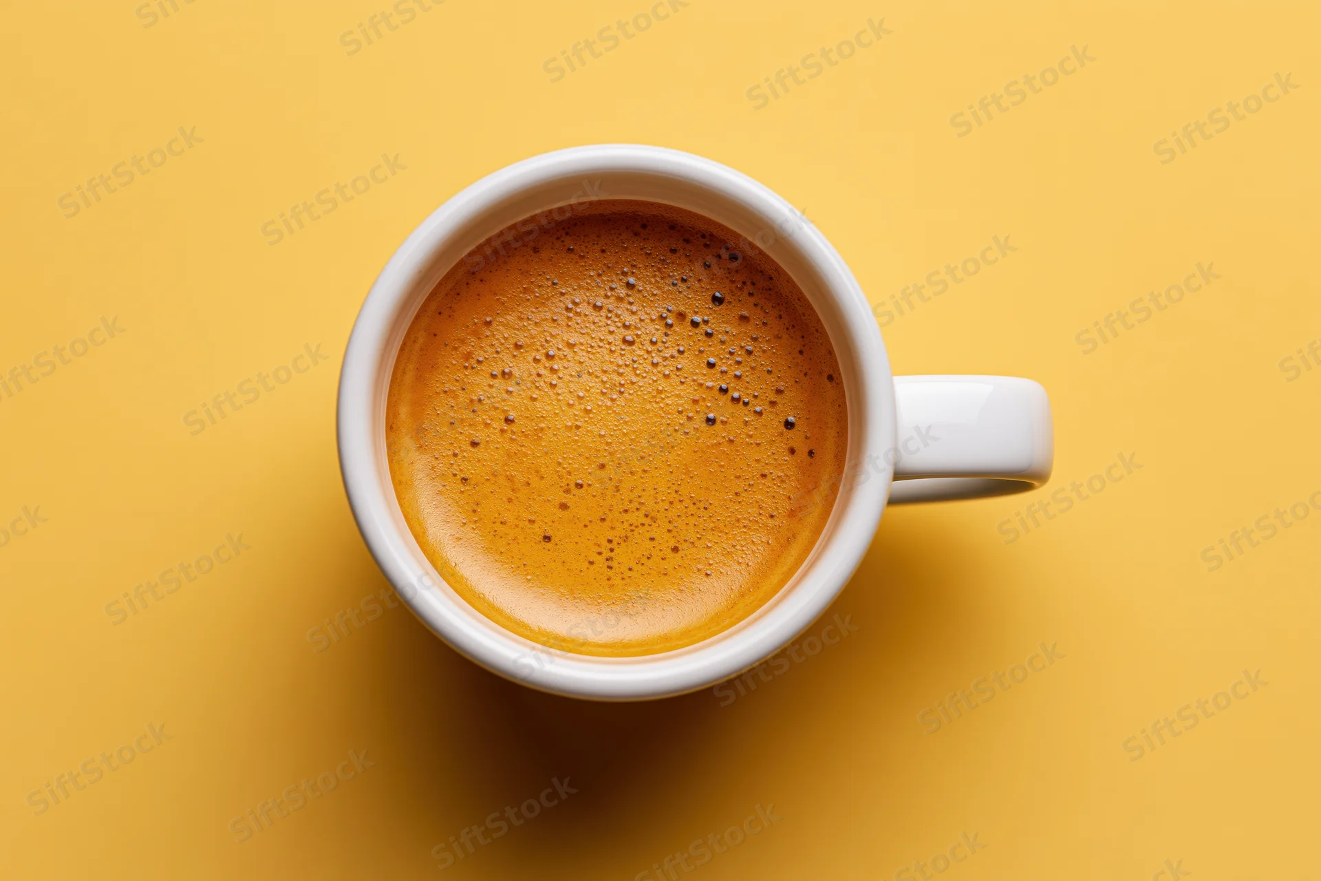 Overhead view of a white ceramic espresso cup filled with frothy coffee on a yellow background