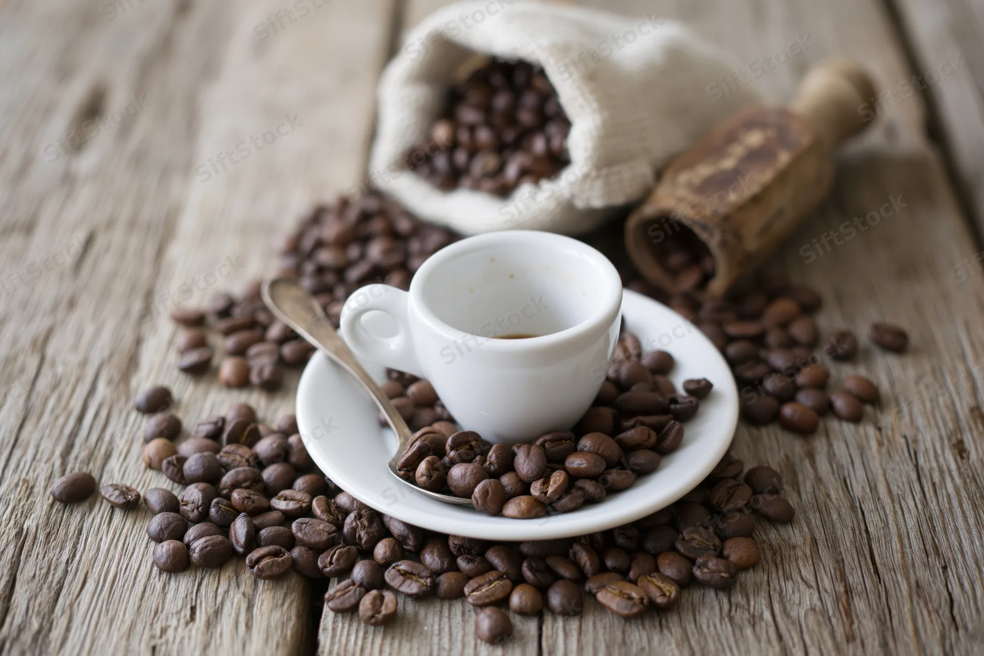 White ceramic espresso cup on saucer with spoon surrounded by coffee beans on wooden table