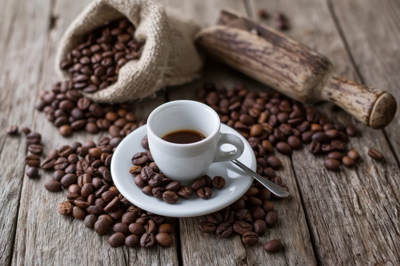 White ceramic espresso cup on saucer with spoon surrounded by coffee beans on rustic wooden table