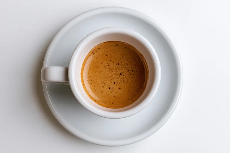 White ceramic espresso cup with crema on matching saucer
