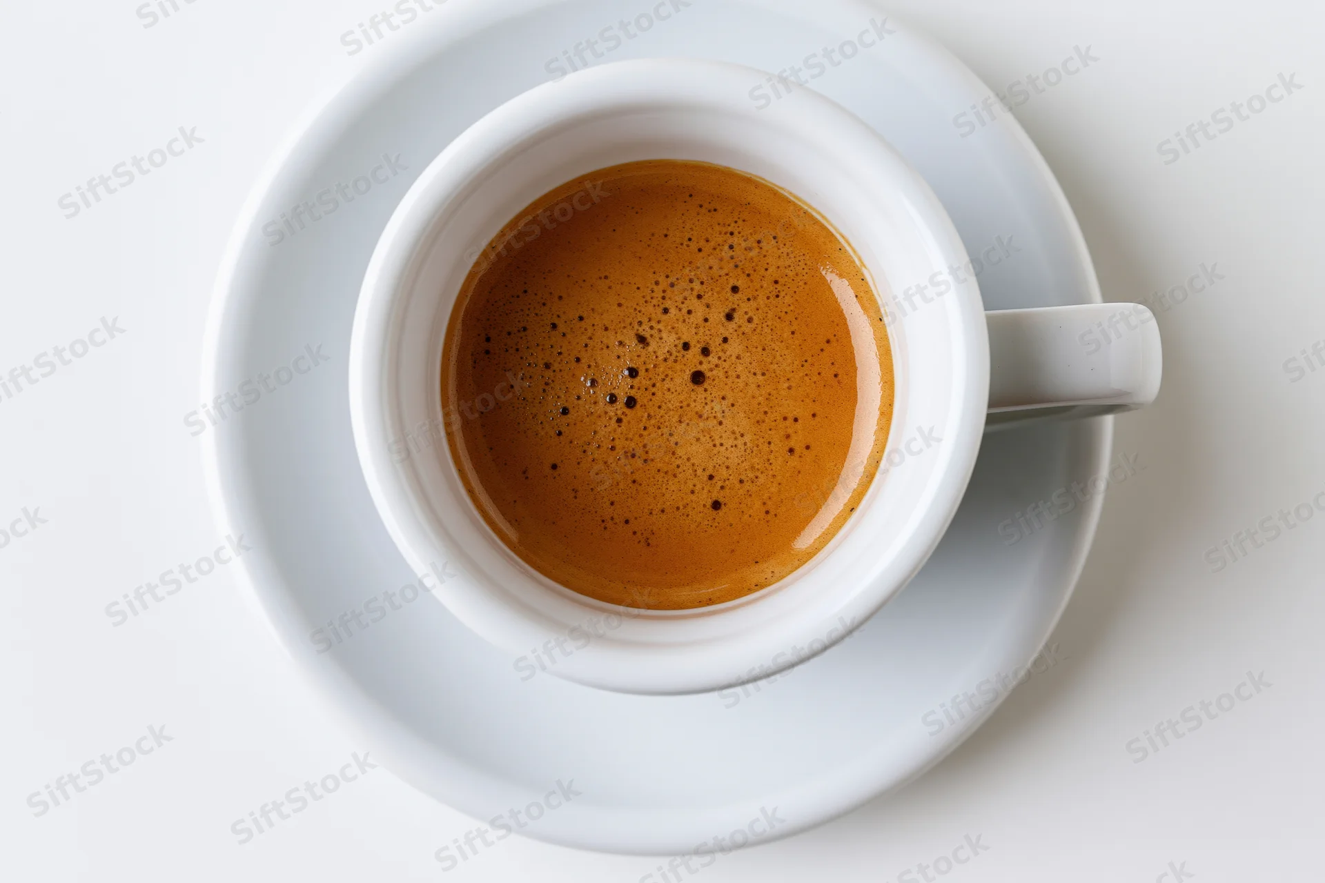 Overhead view of a white ceramic espresso cup with crema on a matching saucer on a white surface