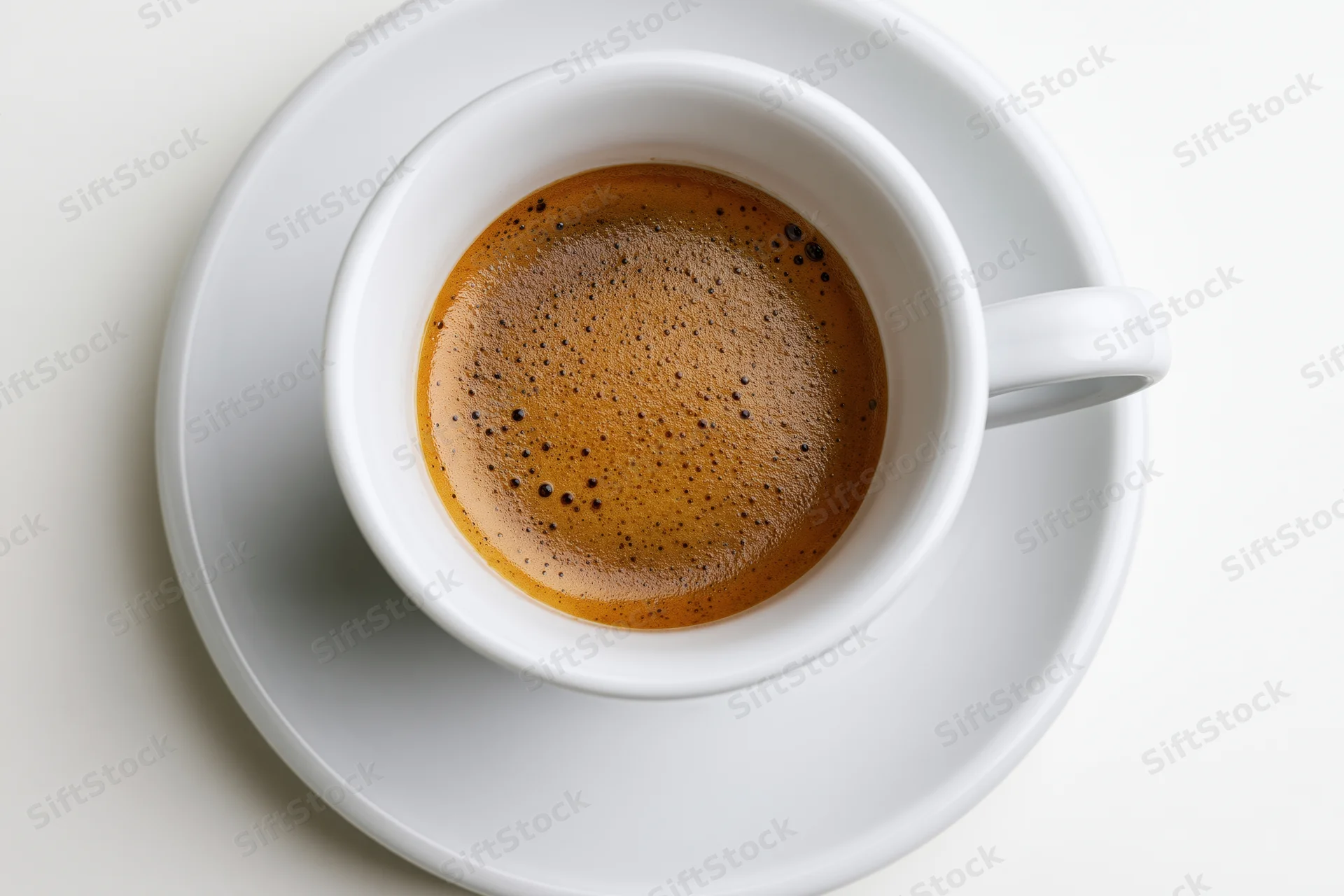 White ceramic espresso cup with crema on matching saucer viewed from above on plain surface