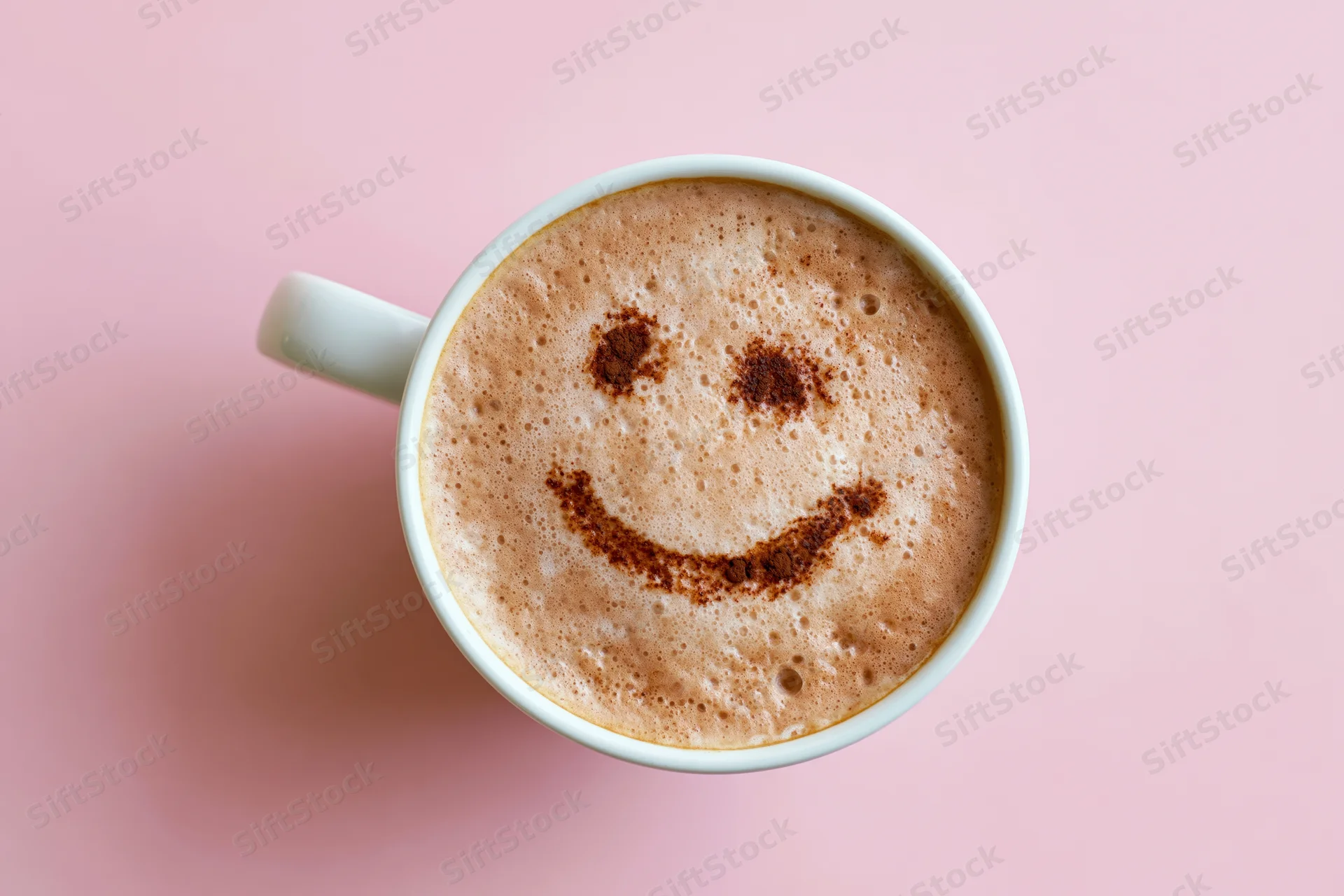 White ceramic mug filled with frothy cappuccino featuring a smiley face made of cinnamon on pink background