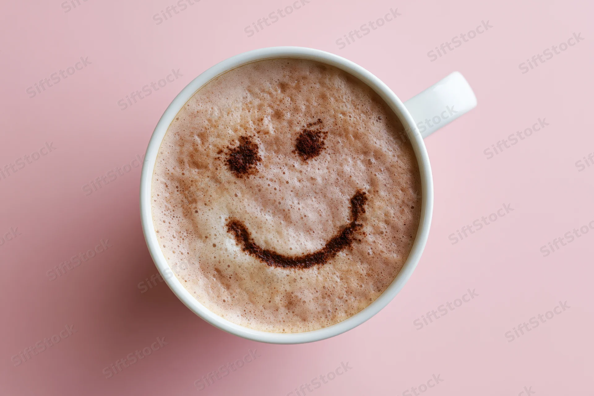 White ceramic mug filled with frothy cappuccino featuring a smiley face made of cocoa powder on pink background