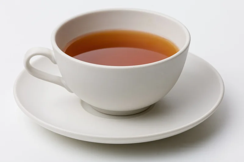 White ceramic tea cup filled with dark brewed tea resting on saucer against plain white background