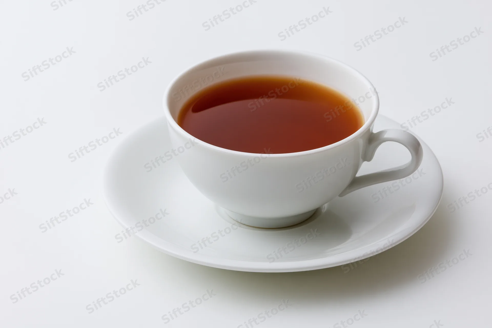 White ceramic tea cup filled with dark brewed tea resting on a matching saucer against a plain white background