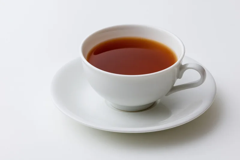 White ceramic tea cup filled with dark brewed tea resting on a matching saucer against a plain white background