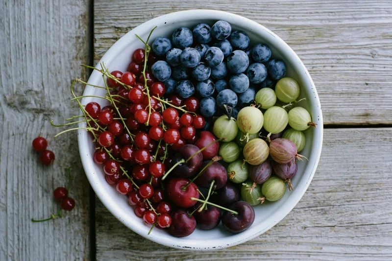 White enamel bowl filled with mixed summer berries on weathered wooden surface