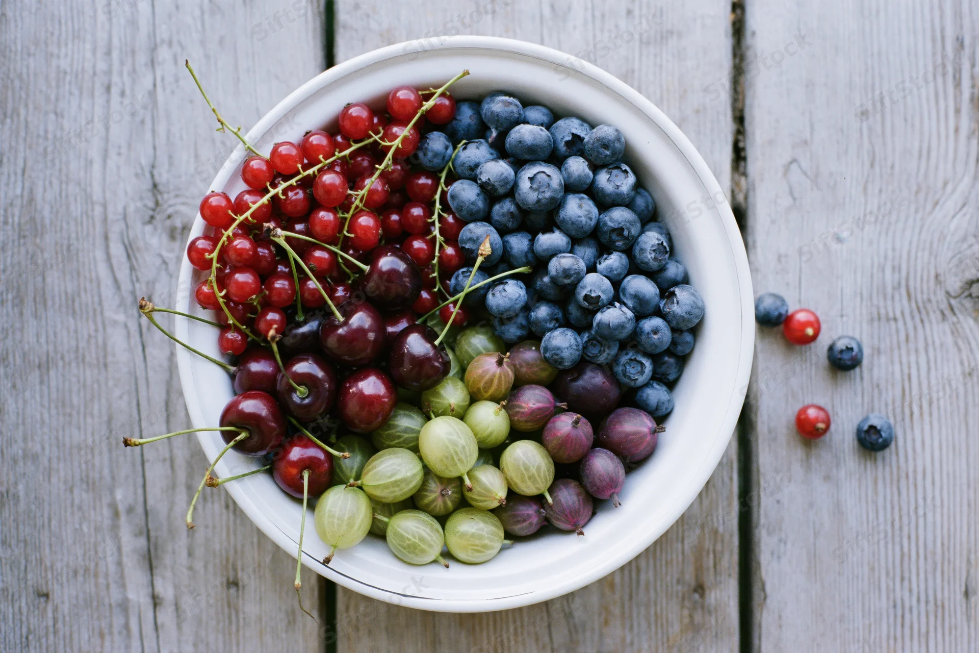 Mixed summer berries in a white enamel bowl on a wooden table