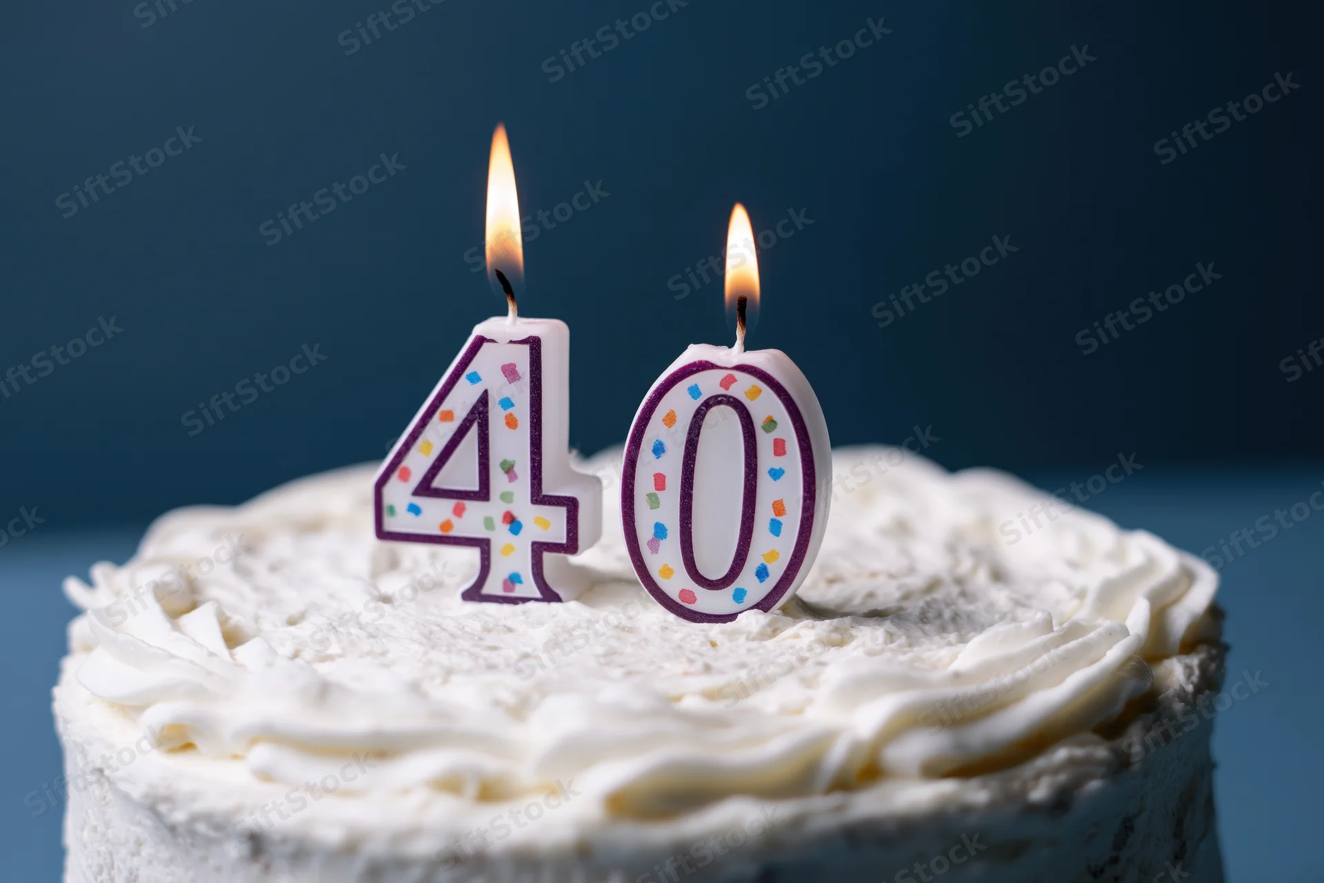 White frosted cake with lit number 40 candles on top
