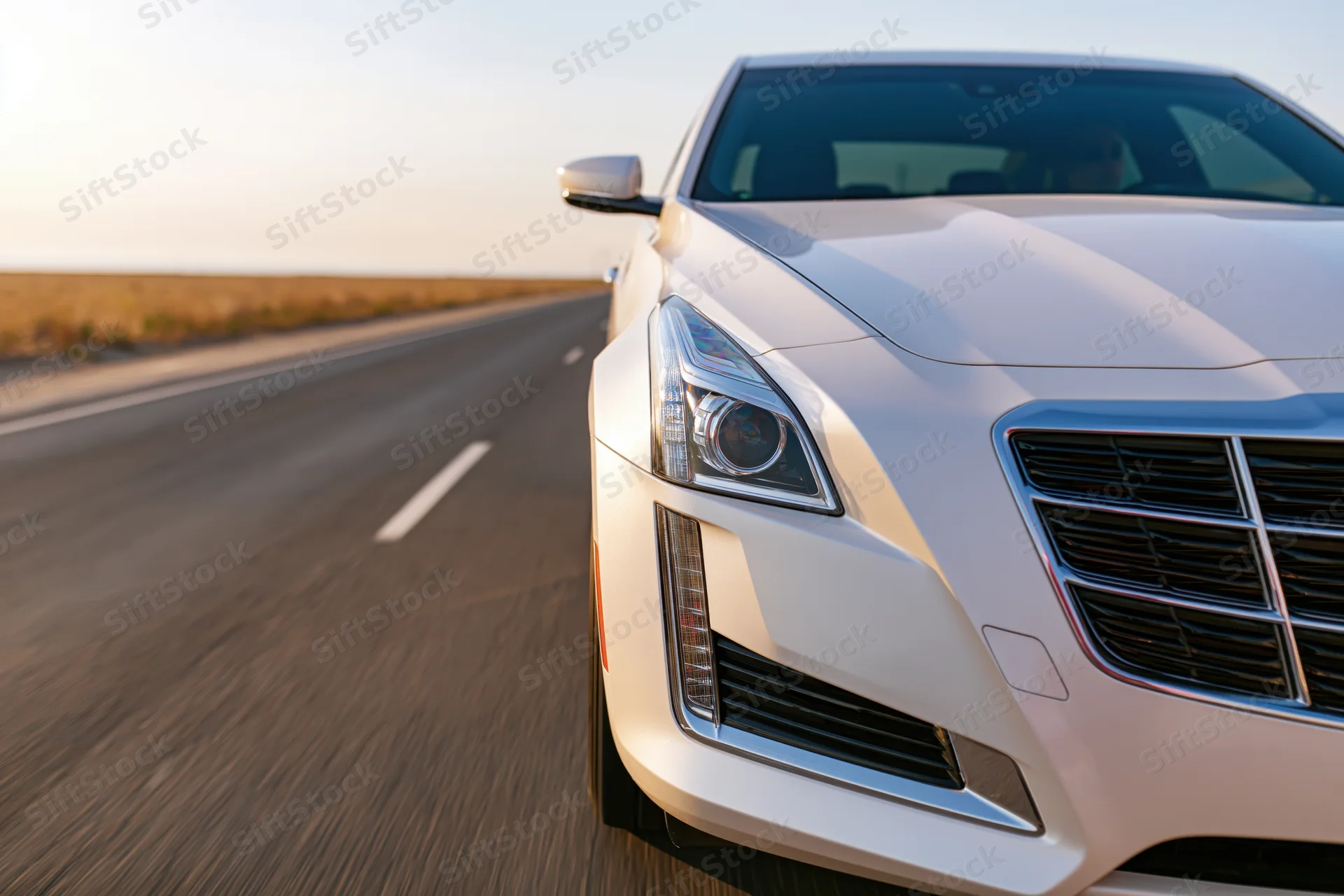 White luxury sedan driving on open two-lane asphalt road with desert landscape in background