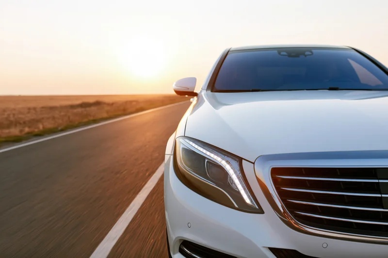 White luxury sedan driving on open two-lane asphalt road at sunset