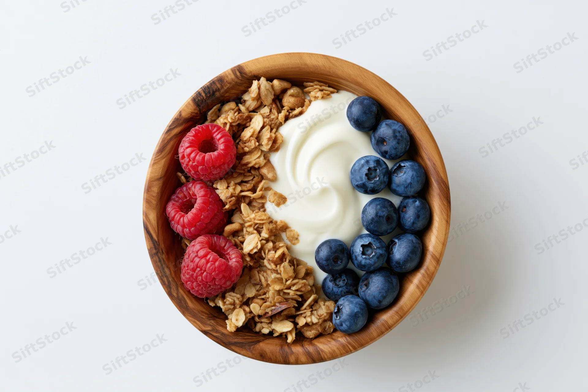 Wooden bowl with yogurt, granola, blueberries and raspberries arranged in sections on white surface