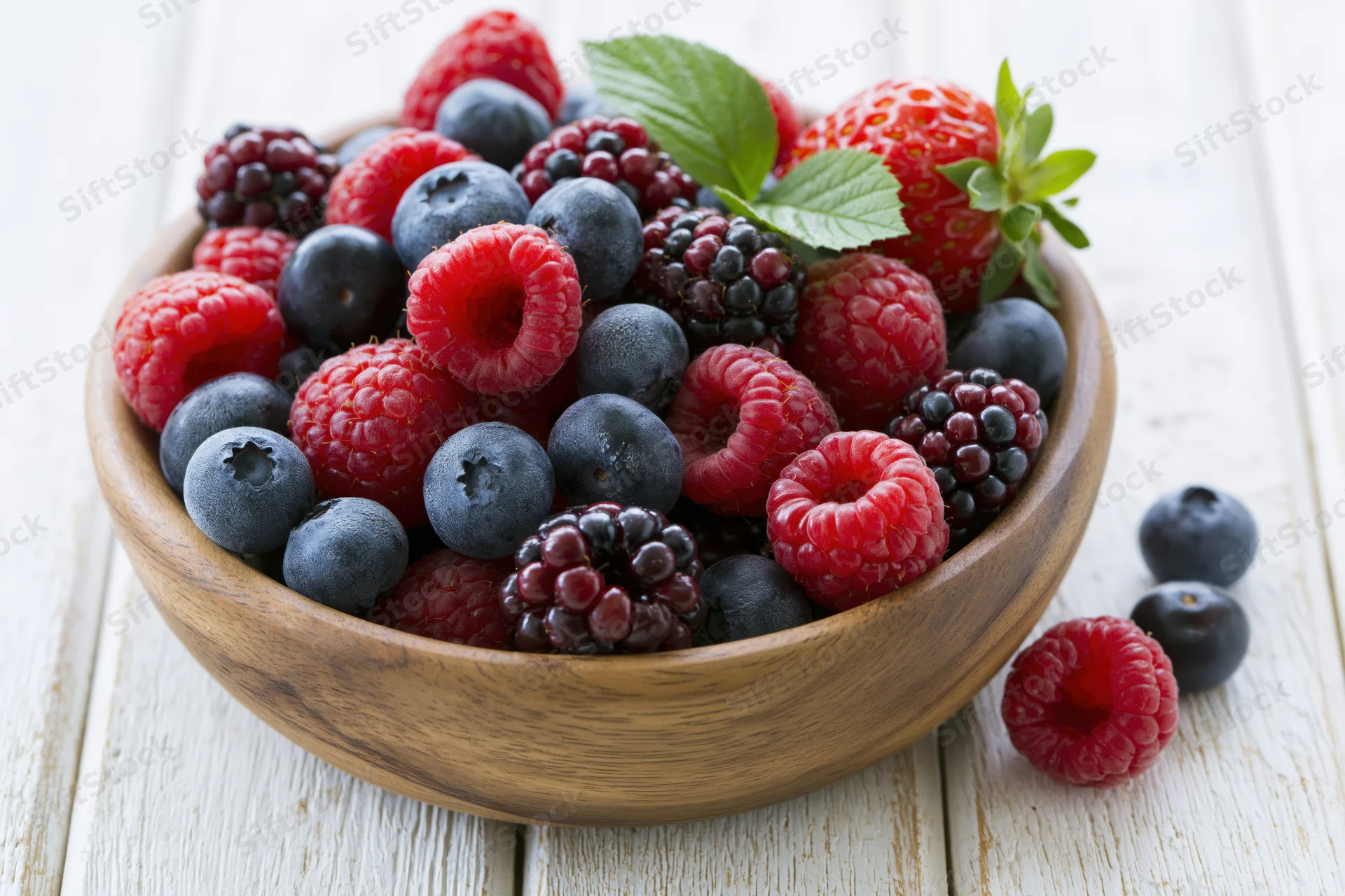 Mixed fresh berries in a wooden bowl on a white wooden surface
