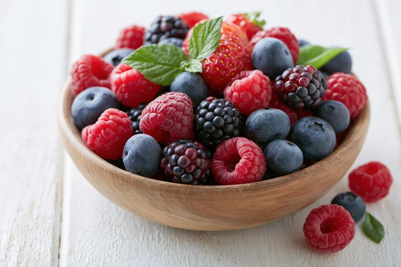 Wooden bowl filled with mixed fresh berries on white wooden surface