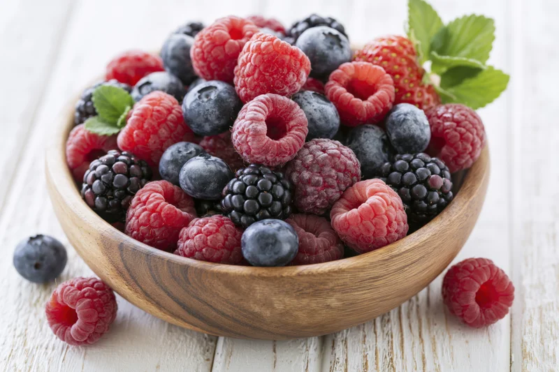 Wooden bowl filled with mixed fresh berries on a white wooden table