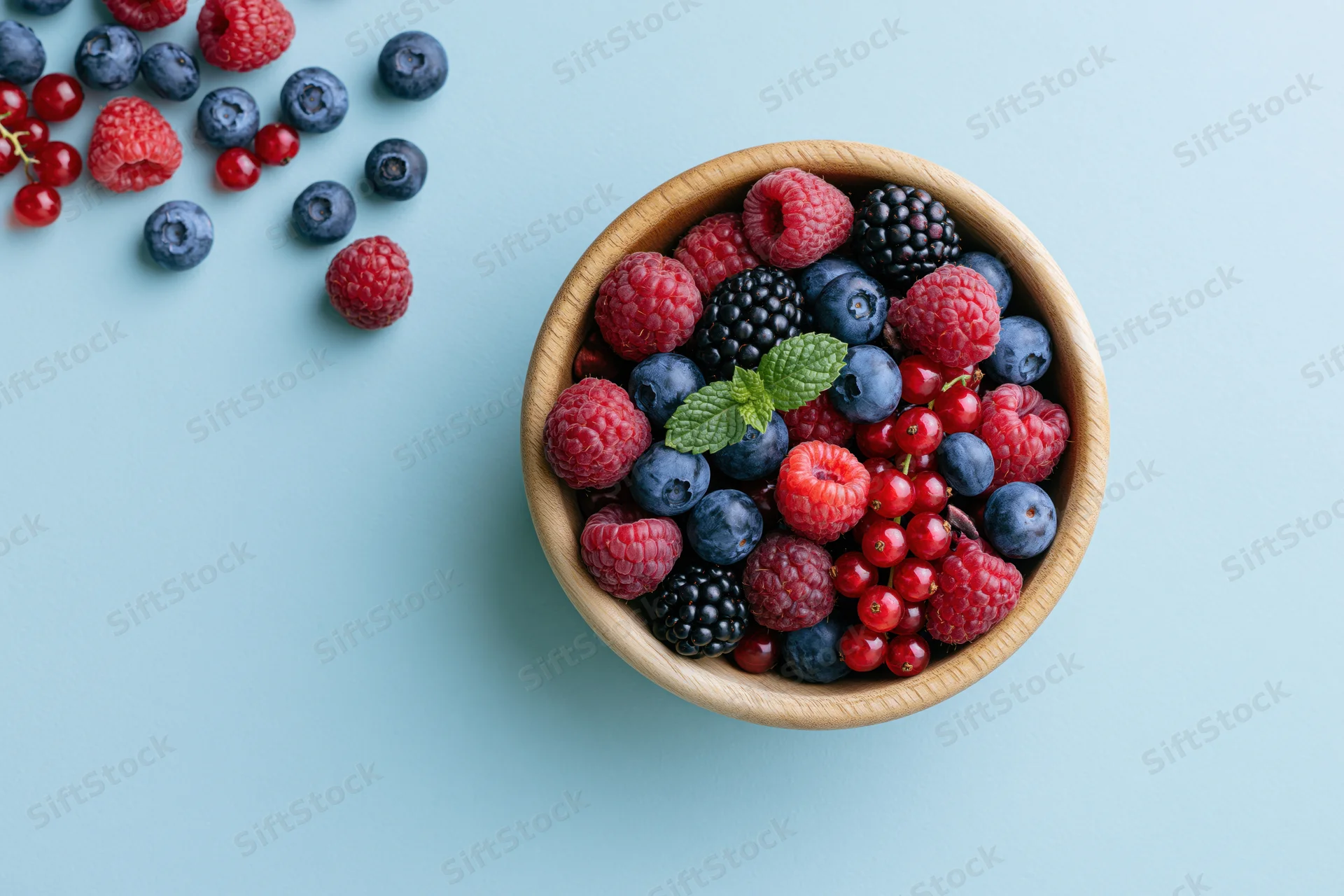 Wooden bowl filled with mixed fresh berries on light blue surface
