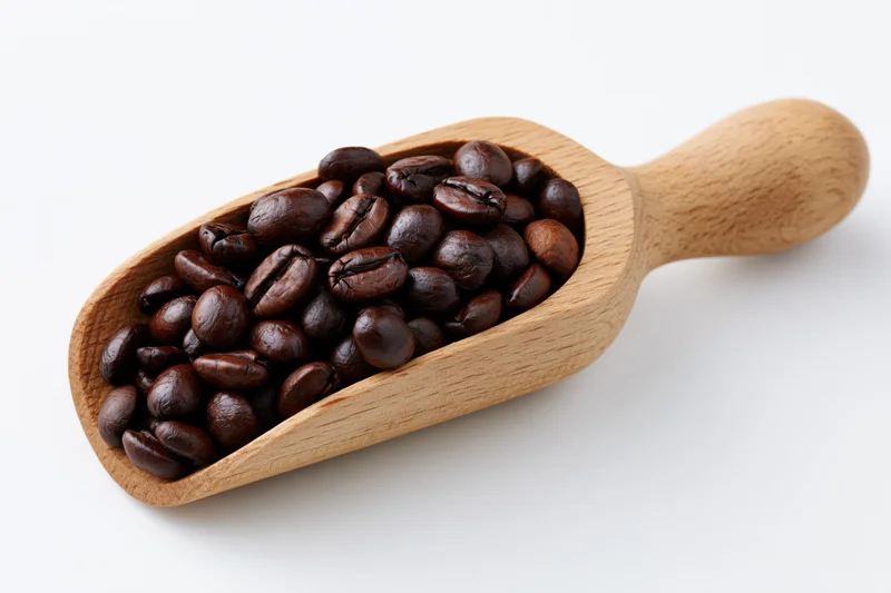 Wooden scoop filled with dark roasted coffee beans on white background