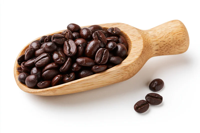Dark roasted coffee beans in a wooden scoop on white background
