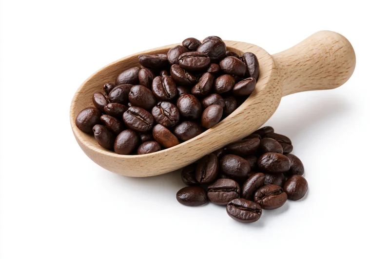 Wooden scoop filled with dark roasted coffee beans spilling onto white surface