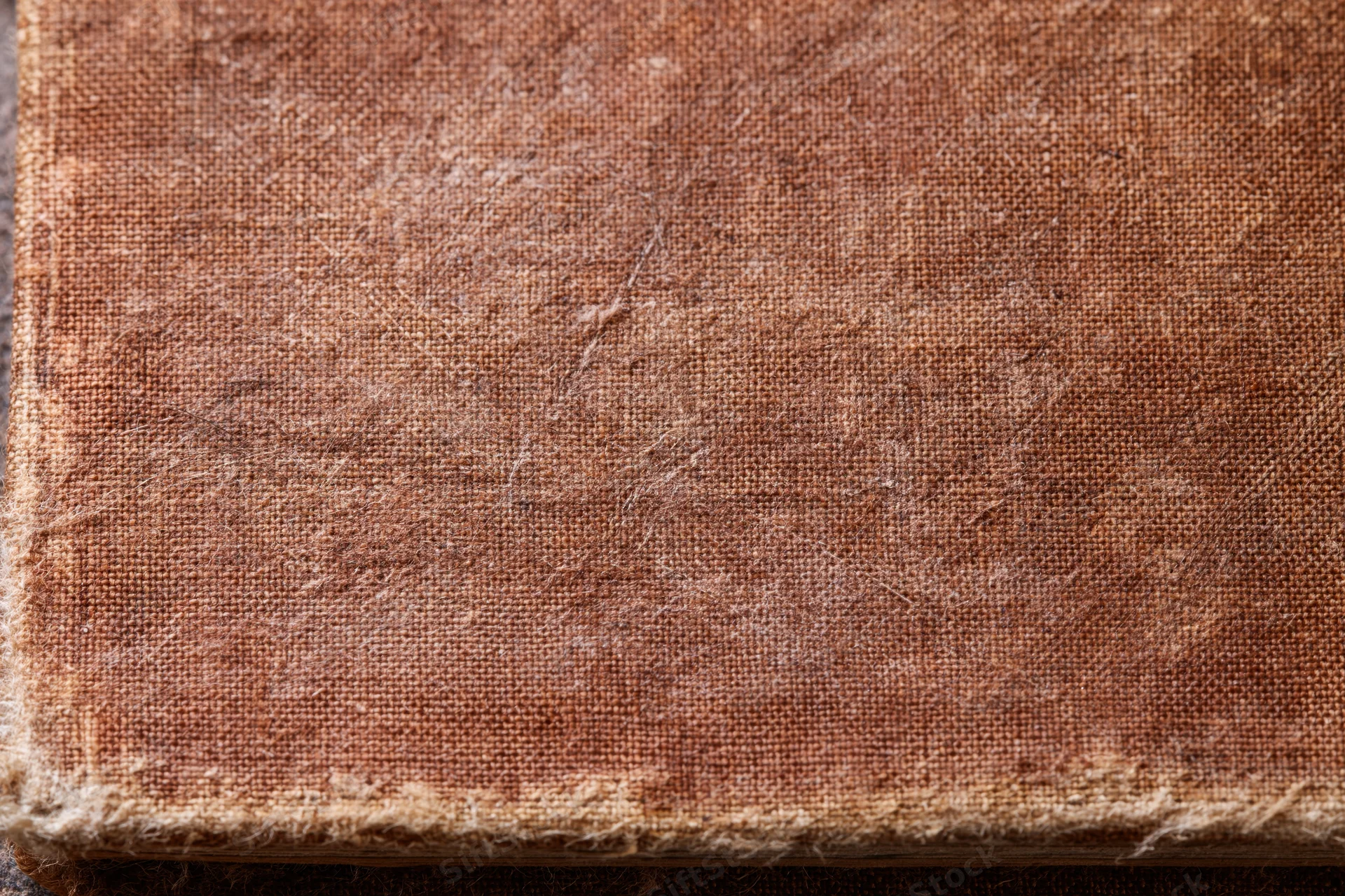 Closeup of worn antique book cover with frayed fabric edge and visible textile texture