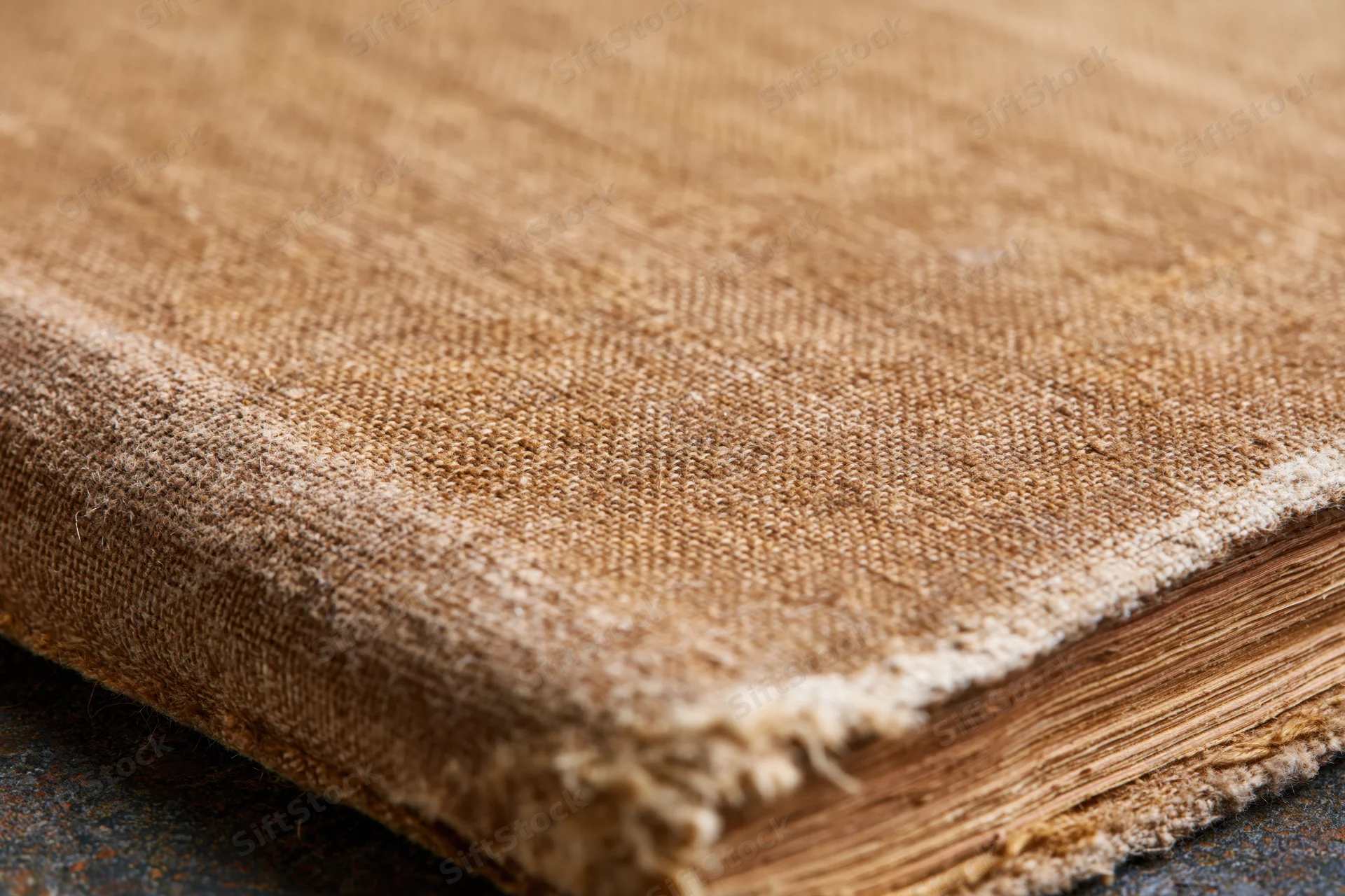 Closeup of worn antique book cover with frayed fabric edge and visible pages