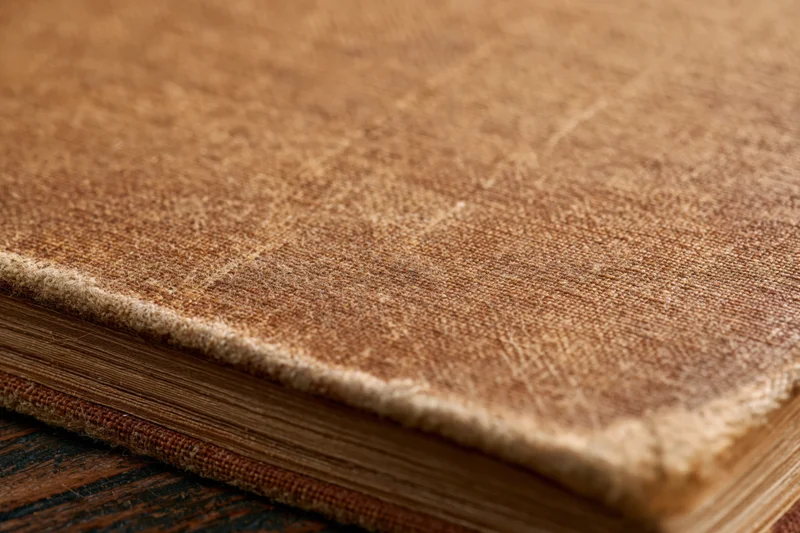 Closeup of worn antique book cover with visible stitching and aged leather texture on dark wooden surface