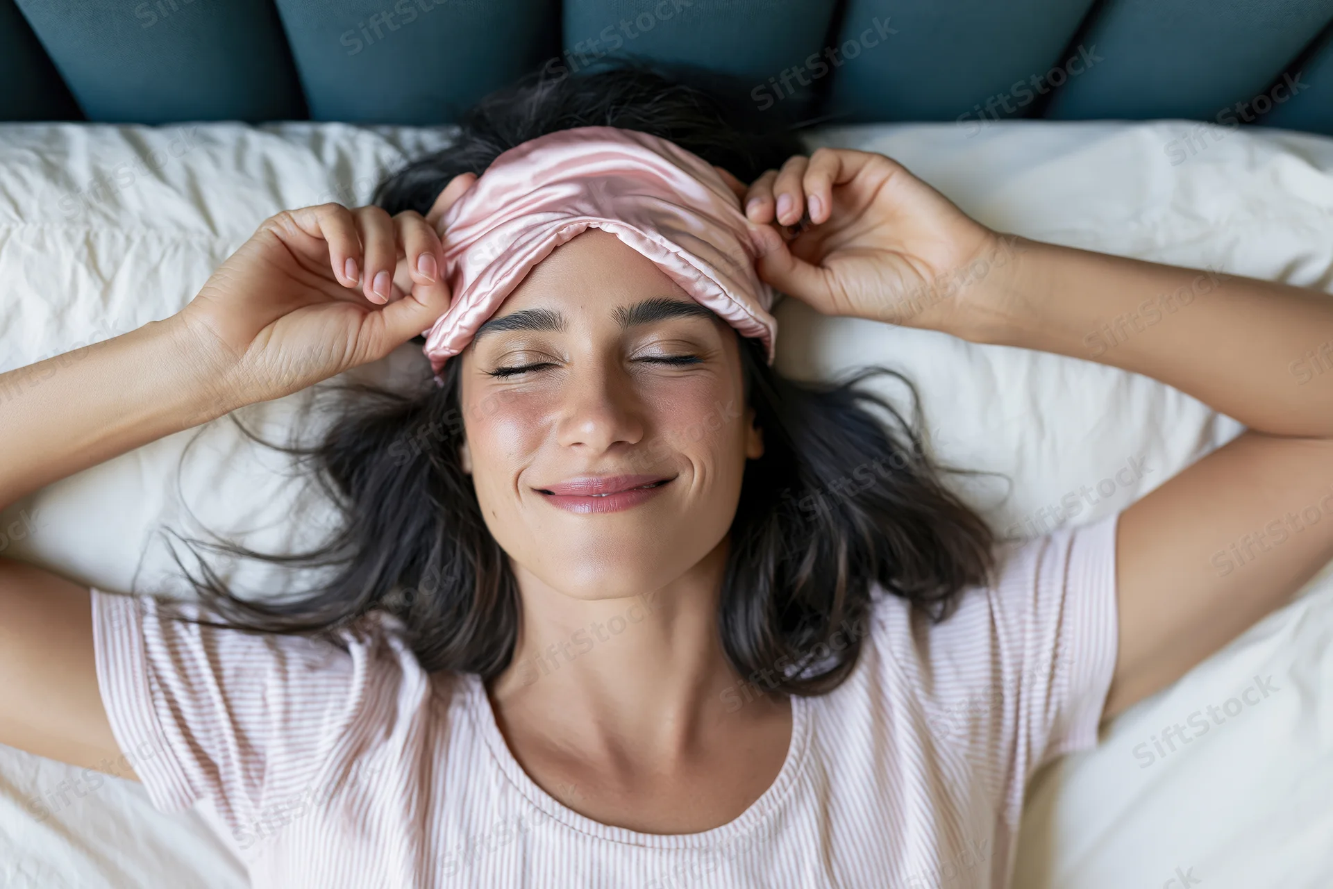 Woman waking in bed smiling with pink satin headband arms raised