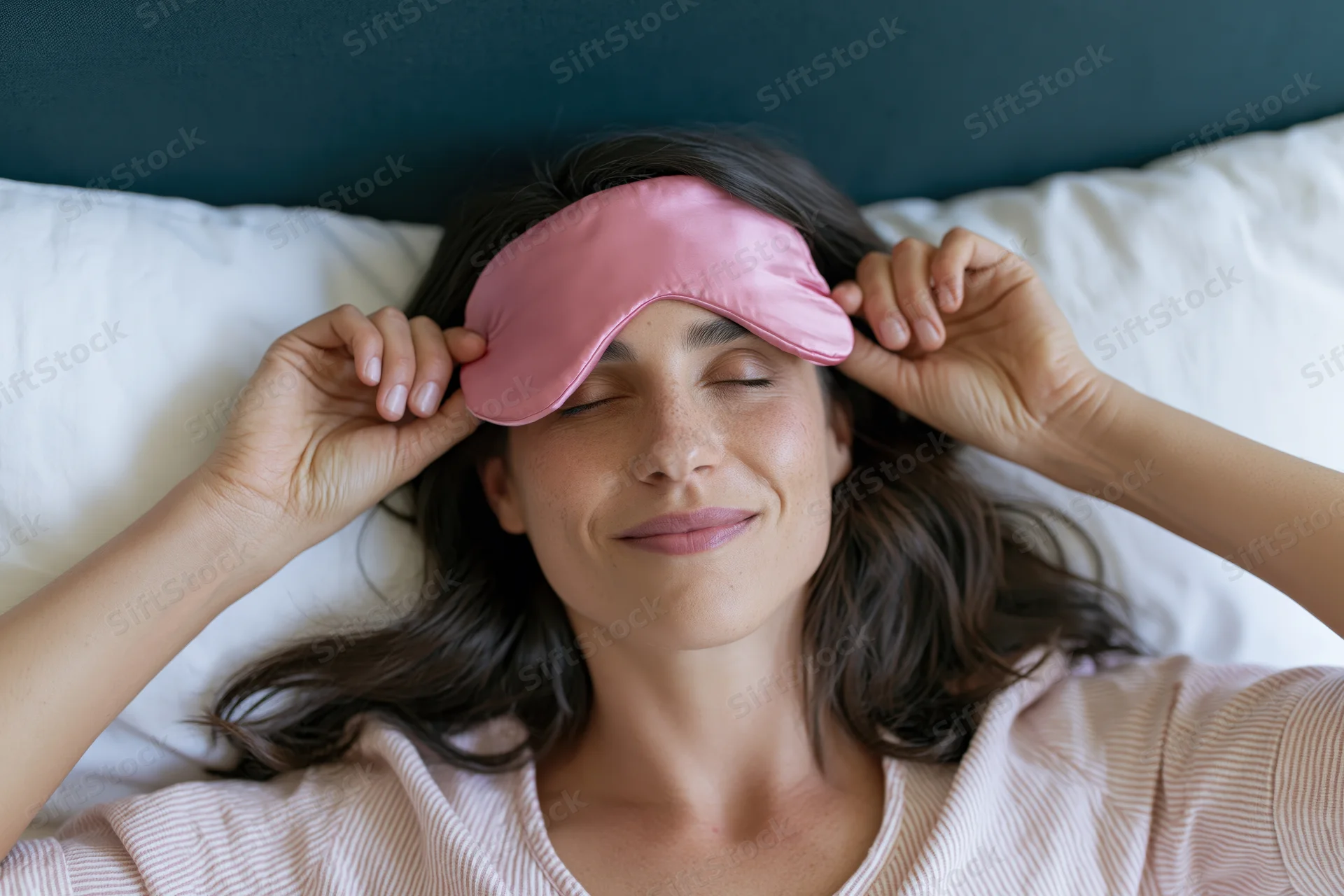 Woman lying in bed lifting pink satin sleep mask in morning