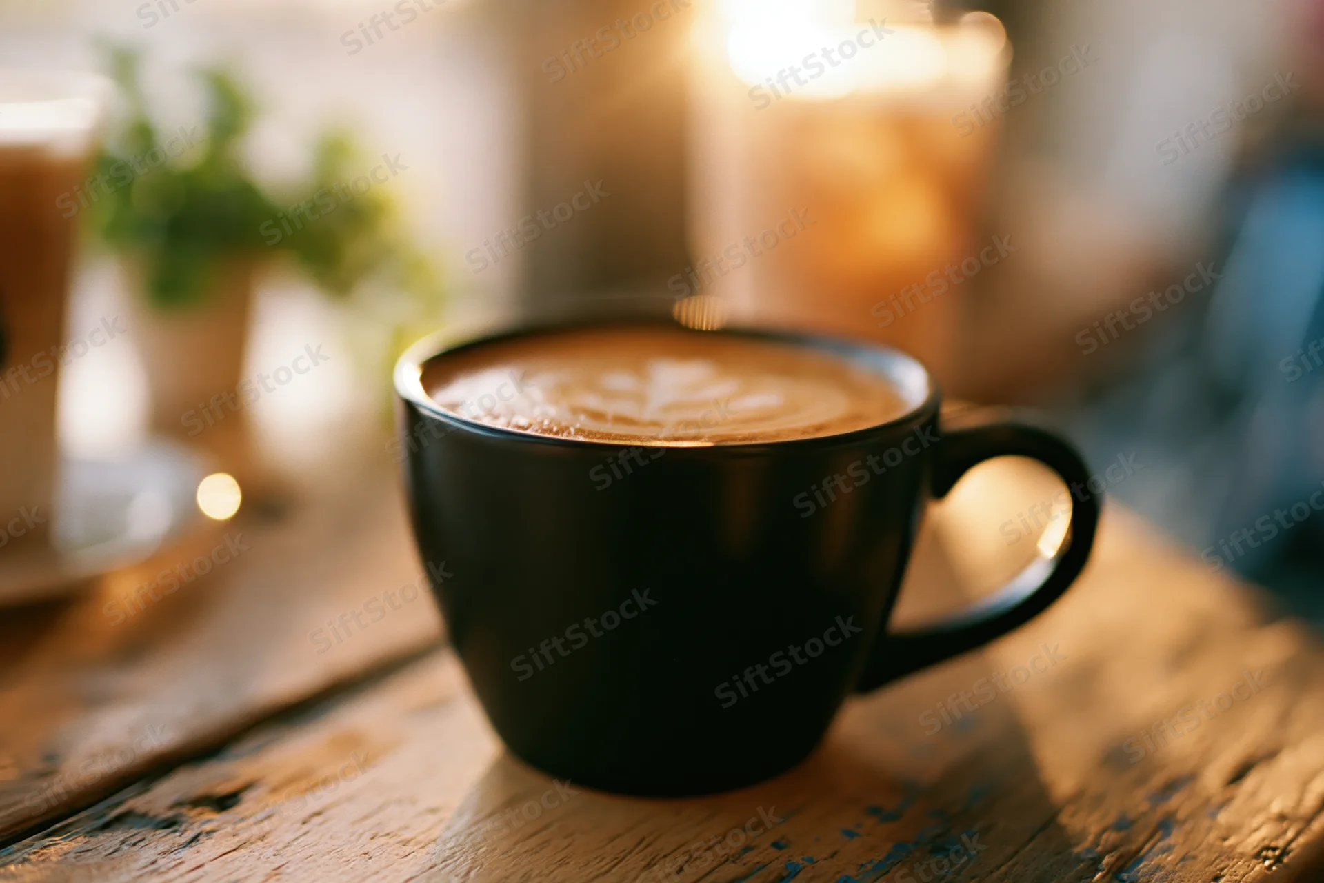 Black ceramic mug with latte art on a worn wooden table in a cozy cafe setting