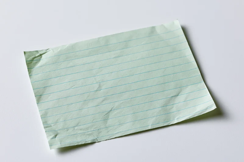 Crumpled pale green ruled index card lying flat on white surface