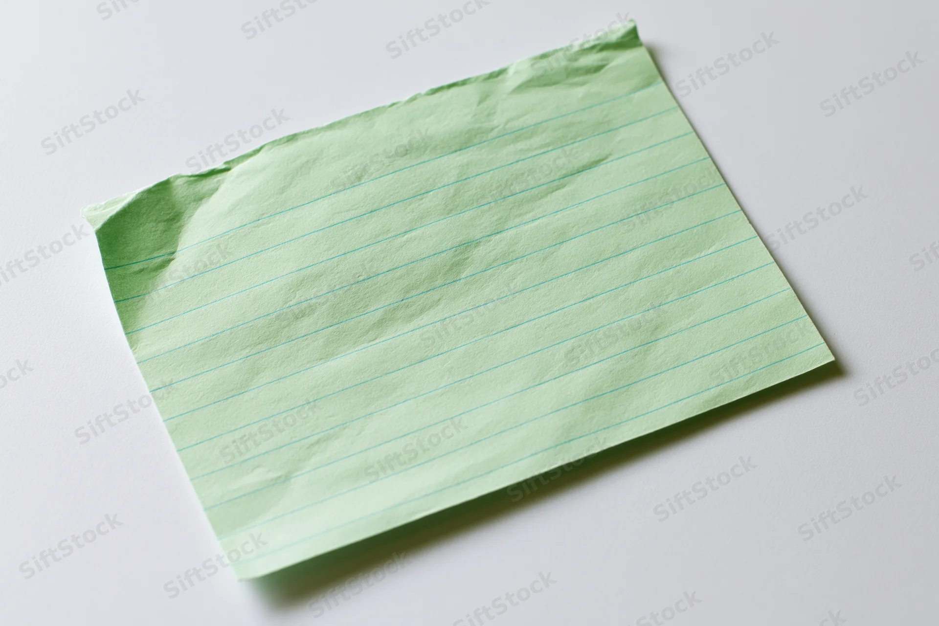 Crumpled pale green ruled index card lying flat on white surface