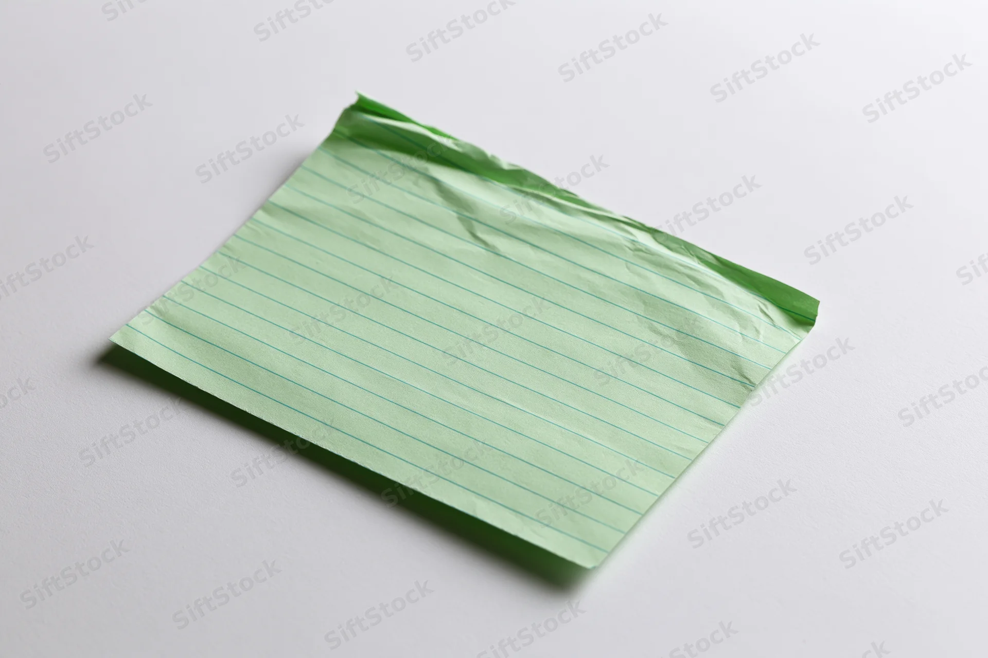 Crumpled pale green lined index card lying flat on white surface