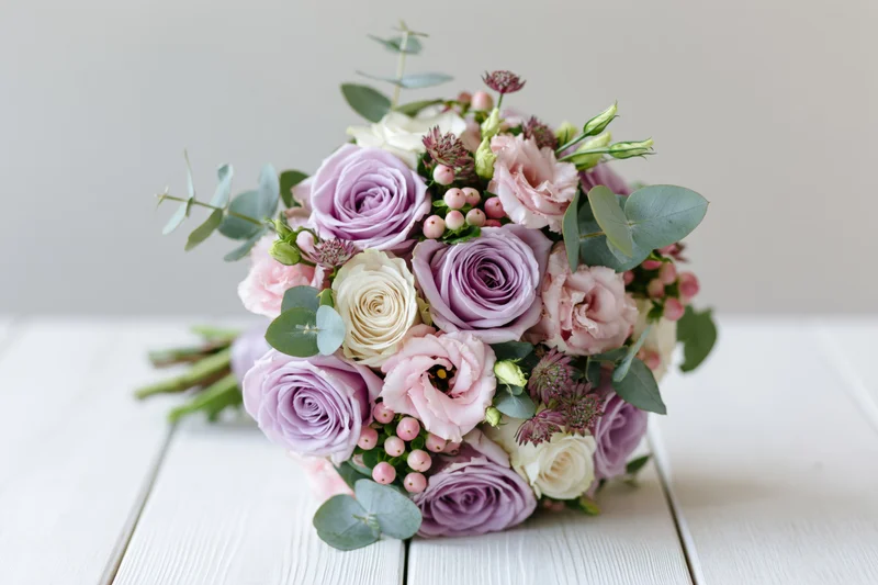 Bridal bouquet with lavender and pink roses and eucalyptus resting on white wooden surface