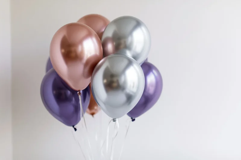 Metallic helium balloons clustered together against a white wall with copyspace