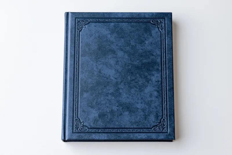 Closed navy blue leather-bound book with embossed decorative border on white background