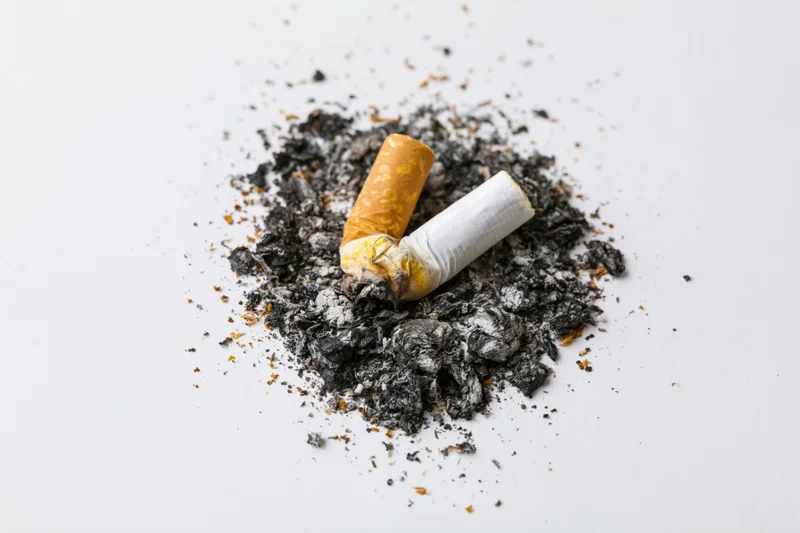 Crushed cigarette butt resting in ash on a white surface
