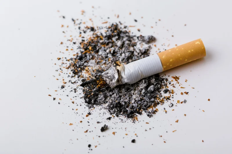 Crushed cigarette butt with ash on white surface