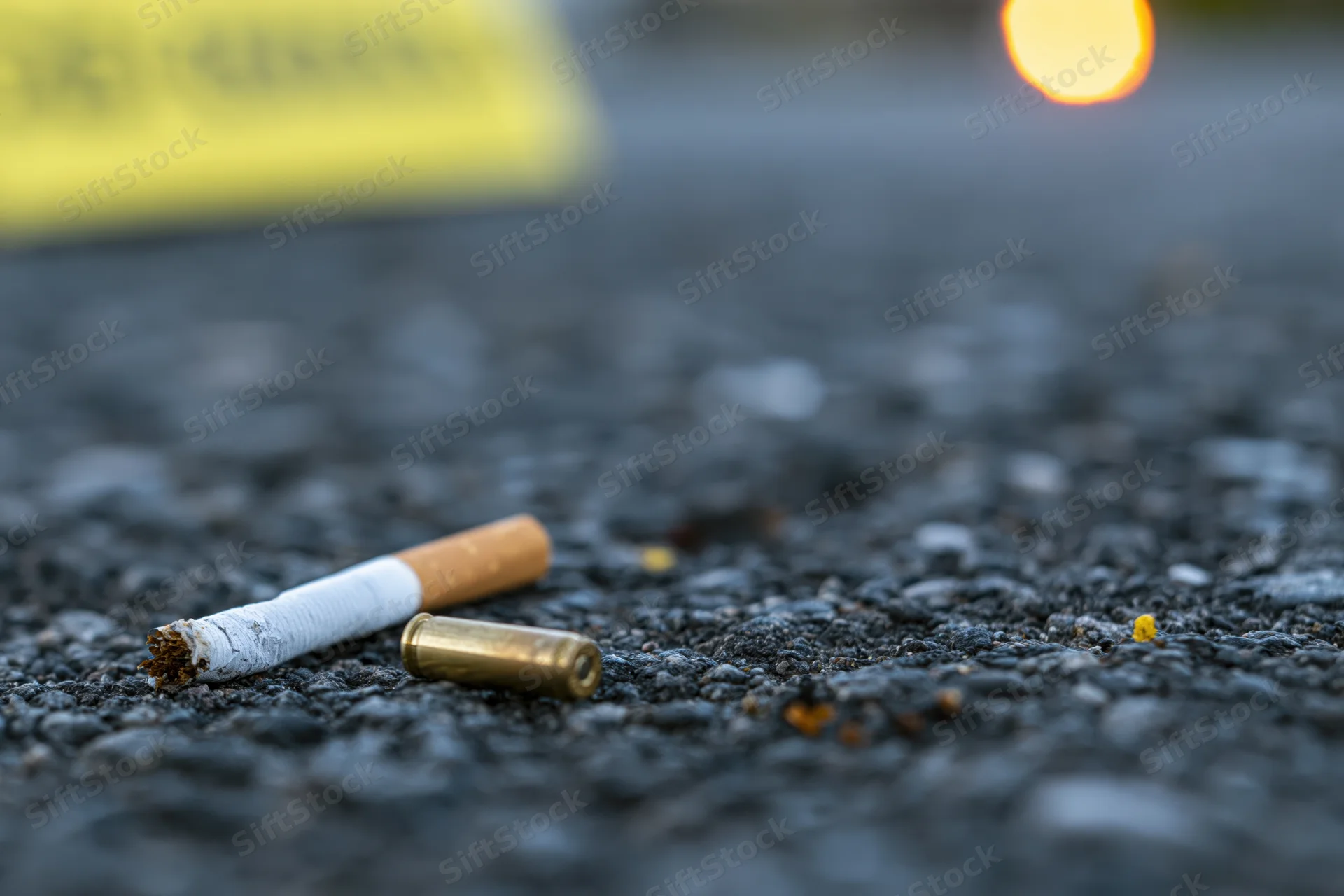 Cigarette butt and bullet casing on asphalt near crime scene tape