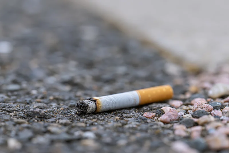 Discarded cigarette butt lying on rough asphalt pavement with gravel and stone fragments