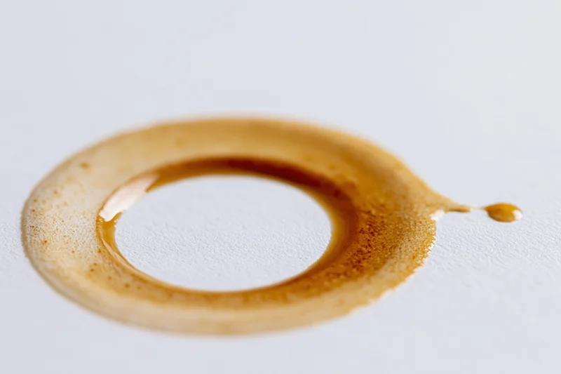 Dried coffee ring stain on a white surface with a drip extending to the side