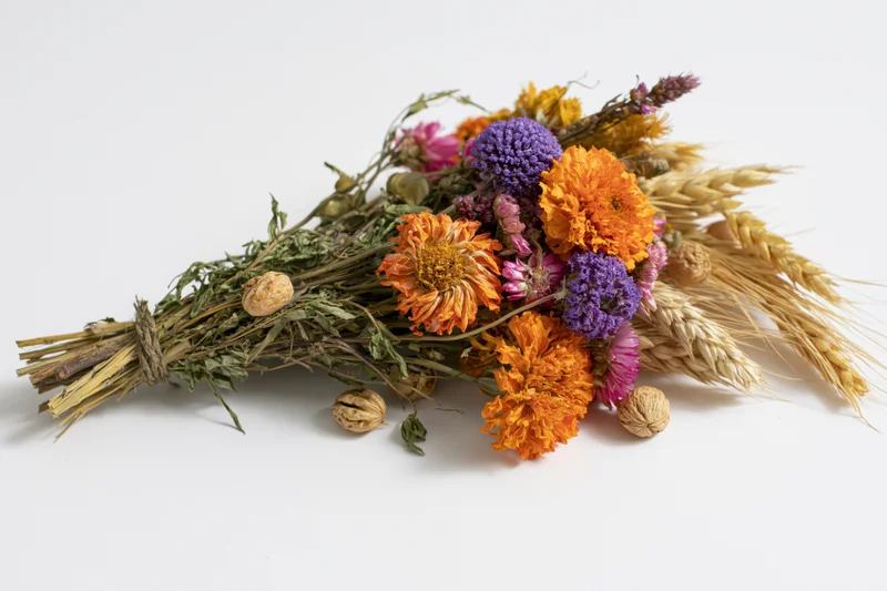 Dried wildflower bouquet with wheat and seedpods lying flat on white surface