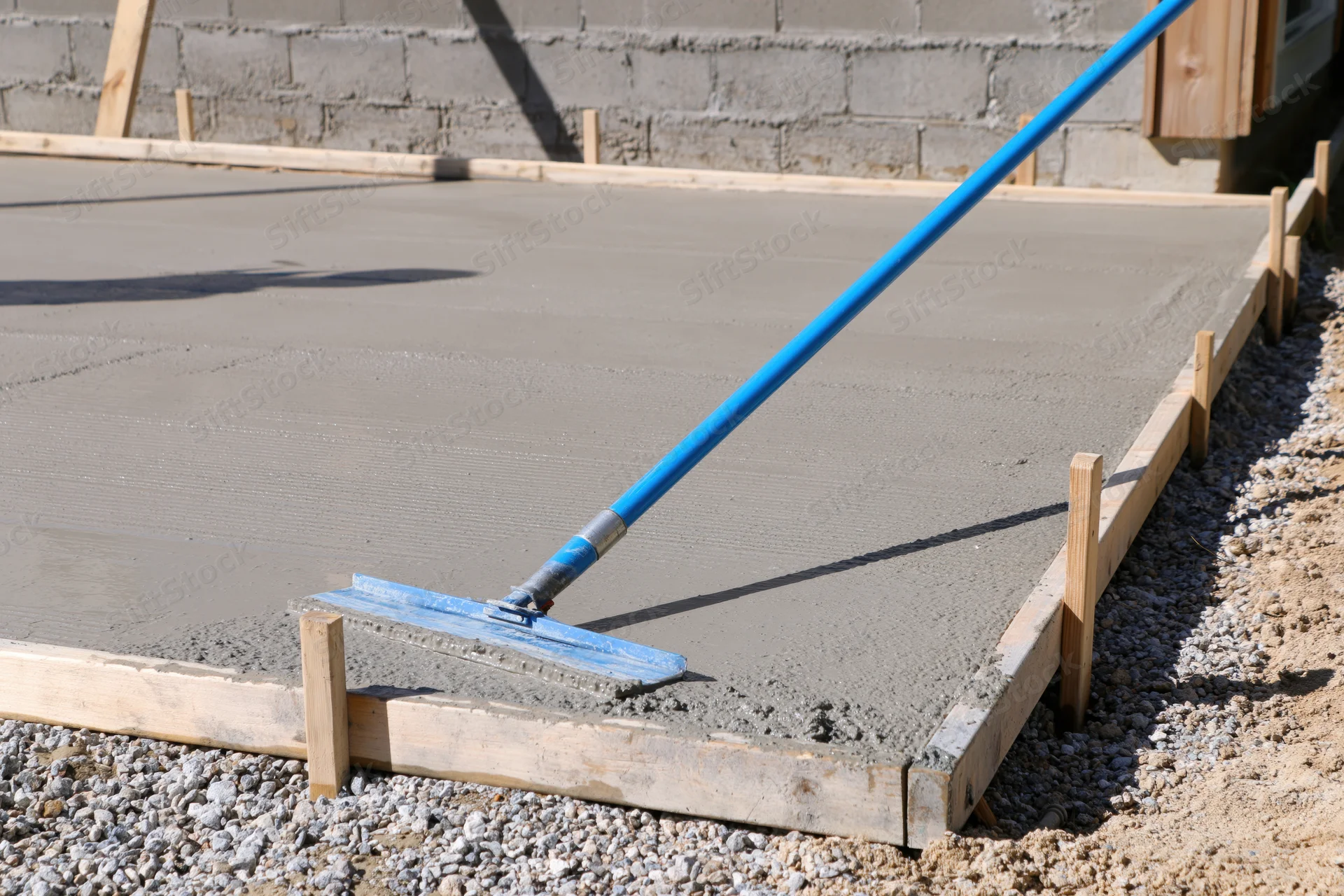 Freshly poured concrete slab being smoothed with a long-handled trowel on a construction site