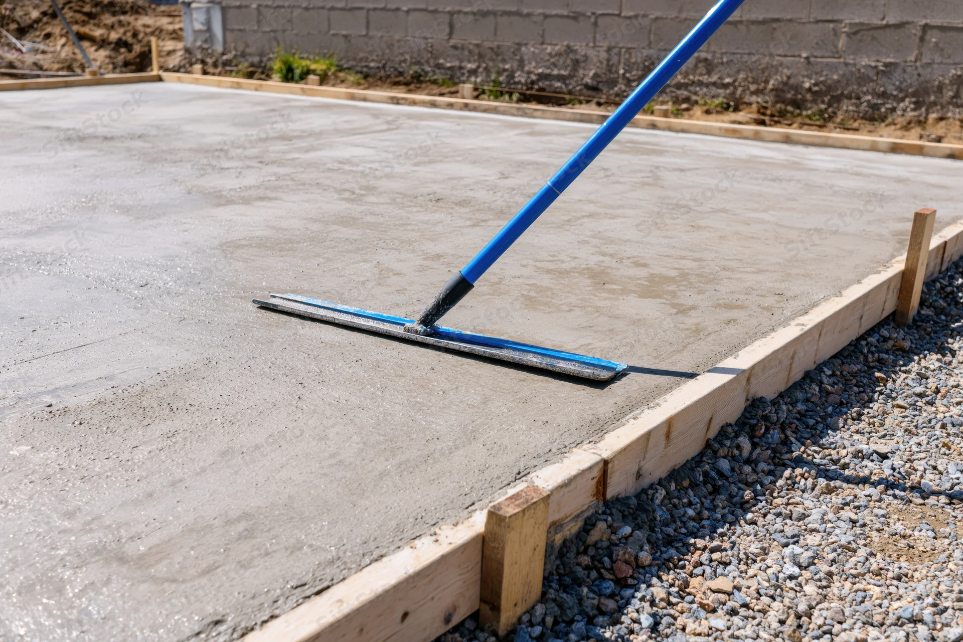 Freshly poured concrete slab being smoothed with a long-handled trowel on a construction site
